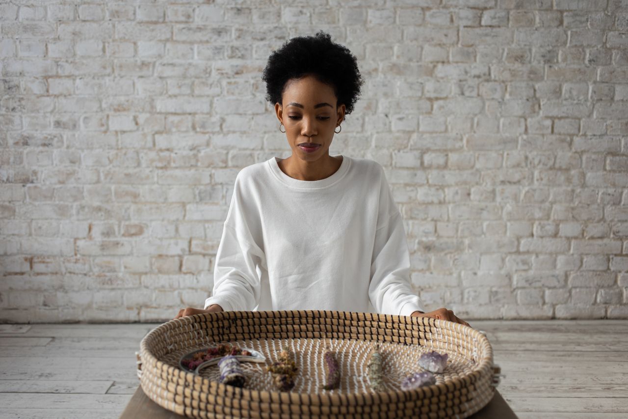 creative-03 A woman in a white sweater meditates with a basket of crystals, symbolizing spirituality and relaxation.