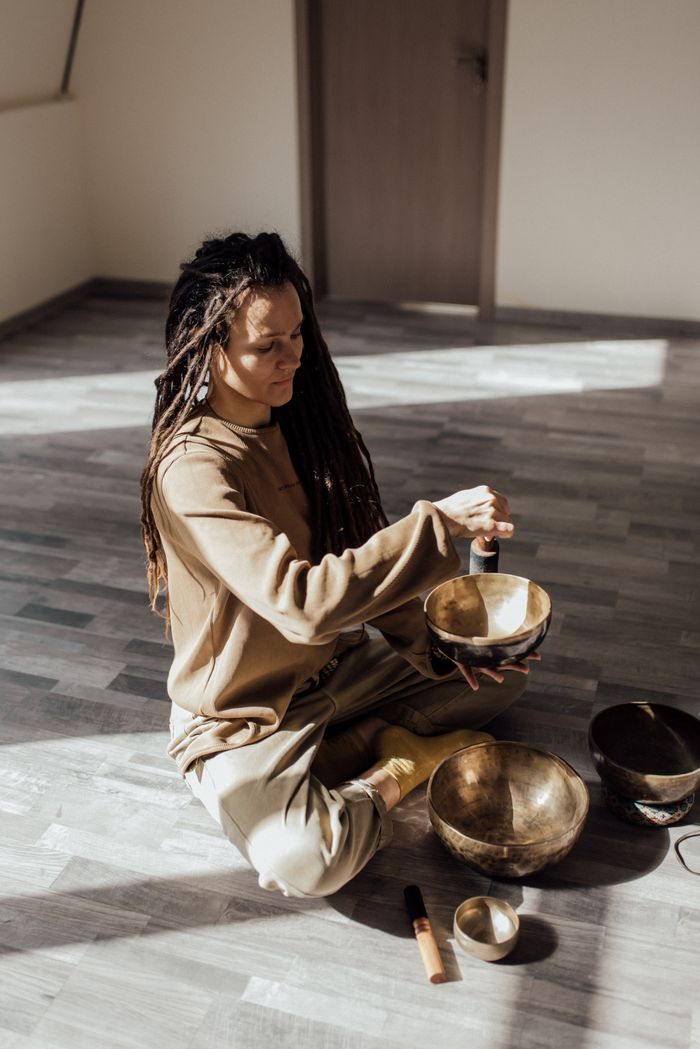 brand-01 Woman meditating indoors with Tibetan singing bowls, promoting relaxation and mindfulness.