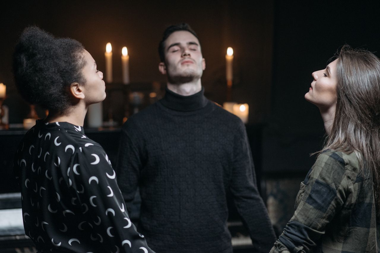 creative-02 Three individuals engage in a spiritual meditation surrounded by candlelight.