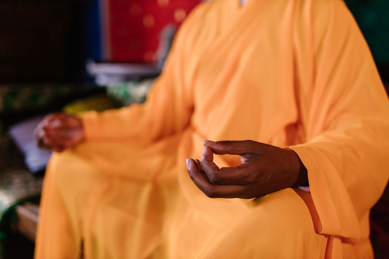 digital-01 Close-up of a meditating monk in traditional orange robe practicing Zen meditation indoors.